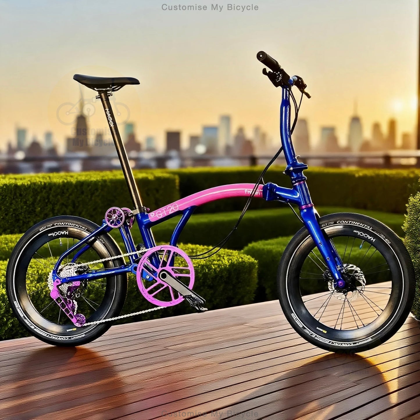 A compact folding bicycle with a metallic blue frame and bright pink accents, parked on a wooden deck with a blurred city skyline and hedges in the background.