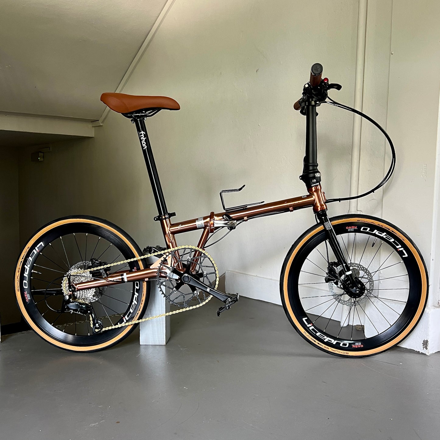 Close-up of titanium gold Fnhon Gust 22” foldie on wooden platform, sunlight reflecting off the polished frame.
