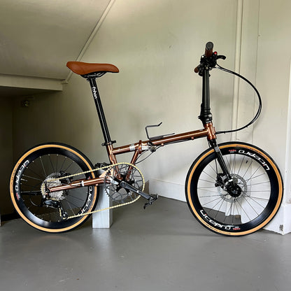 Close-up of titanium gold Fnhon Gust 22” foldie on wooden platform, sunlight reflecting off the polished frame.
