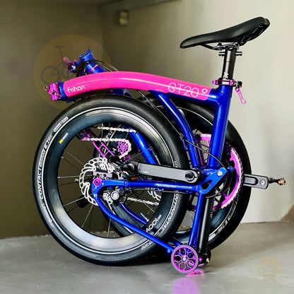 A folded bicycle with a bright blue frame and vivid pink fenders, shown standing indoors on its rear wheel. The bike has visible branding including 'fnhon' on the top tube and 'Continental' on the tire sidewall.
