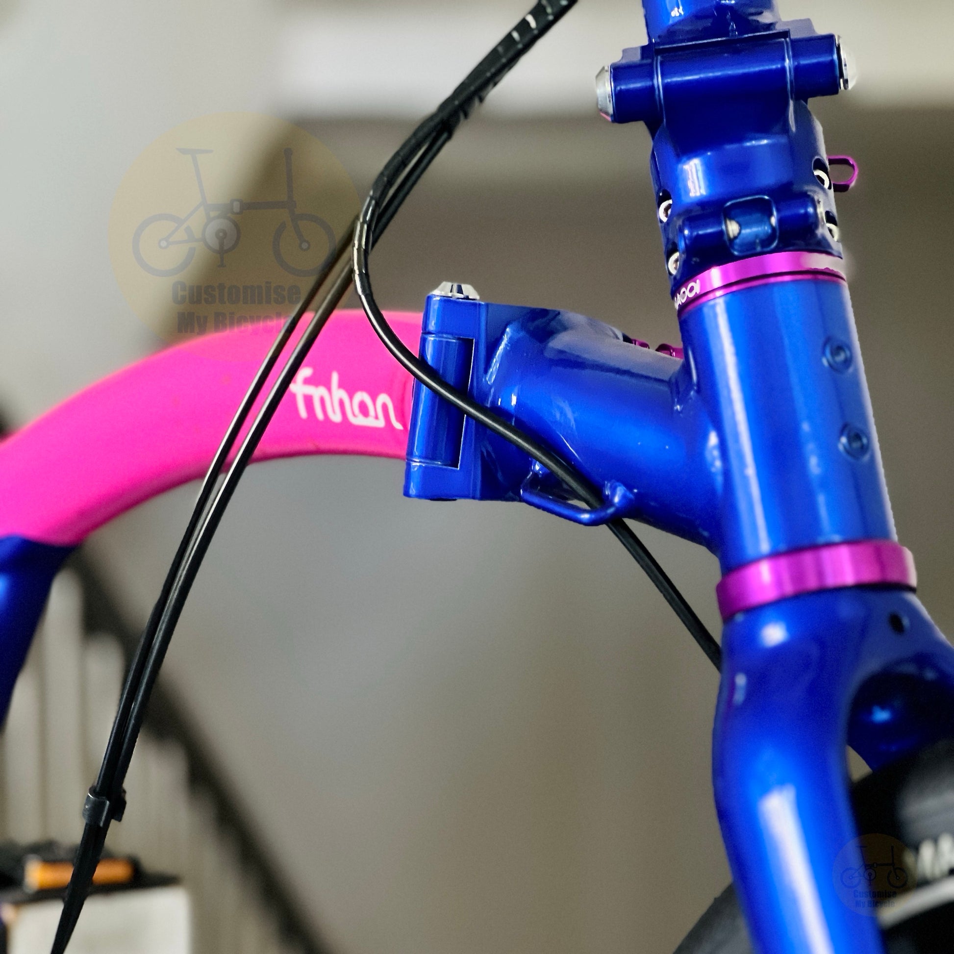 Close-up of a bicycle frame with a bright blue metallic finish and magenta pink accents, including a pink wheel rim and black brake cables.