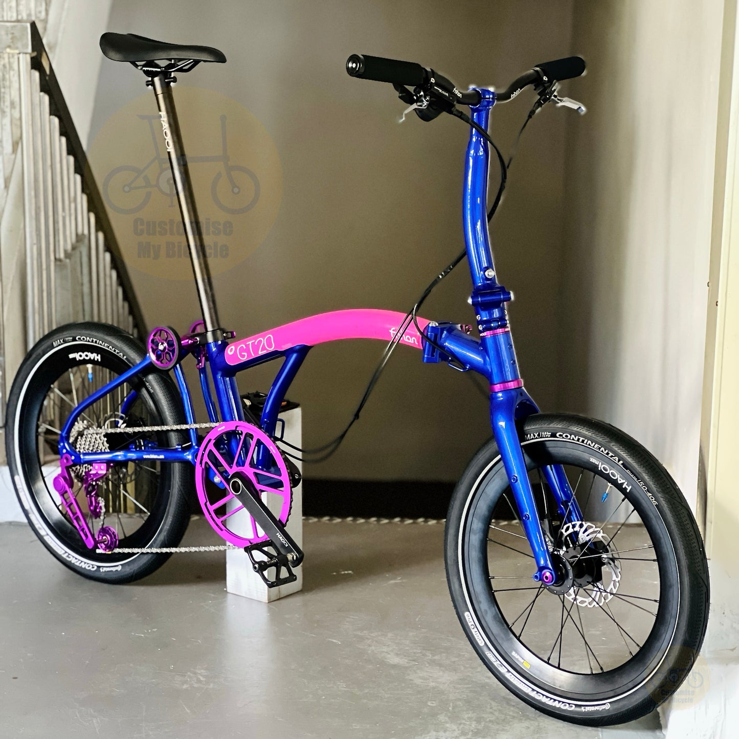 A compact folding bicycle fnhon GT20 with a vibrant blue frame and bright pink accents, including the seat tube and handlebar area, parked indoors on a concrete floor next to a staircase.