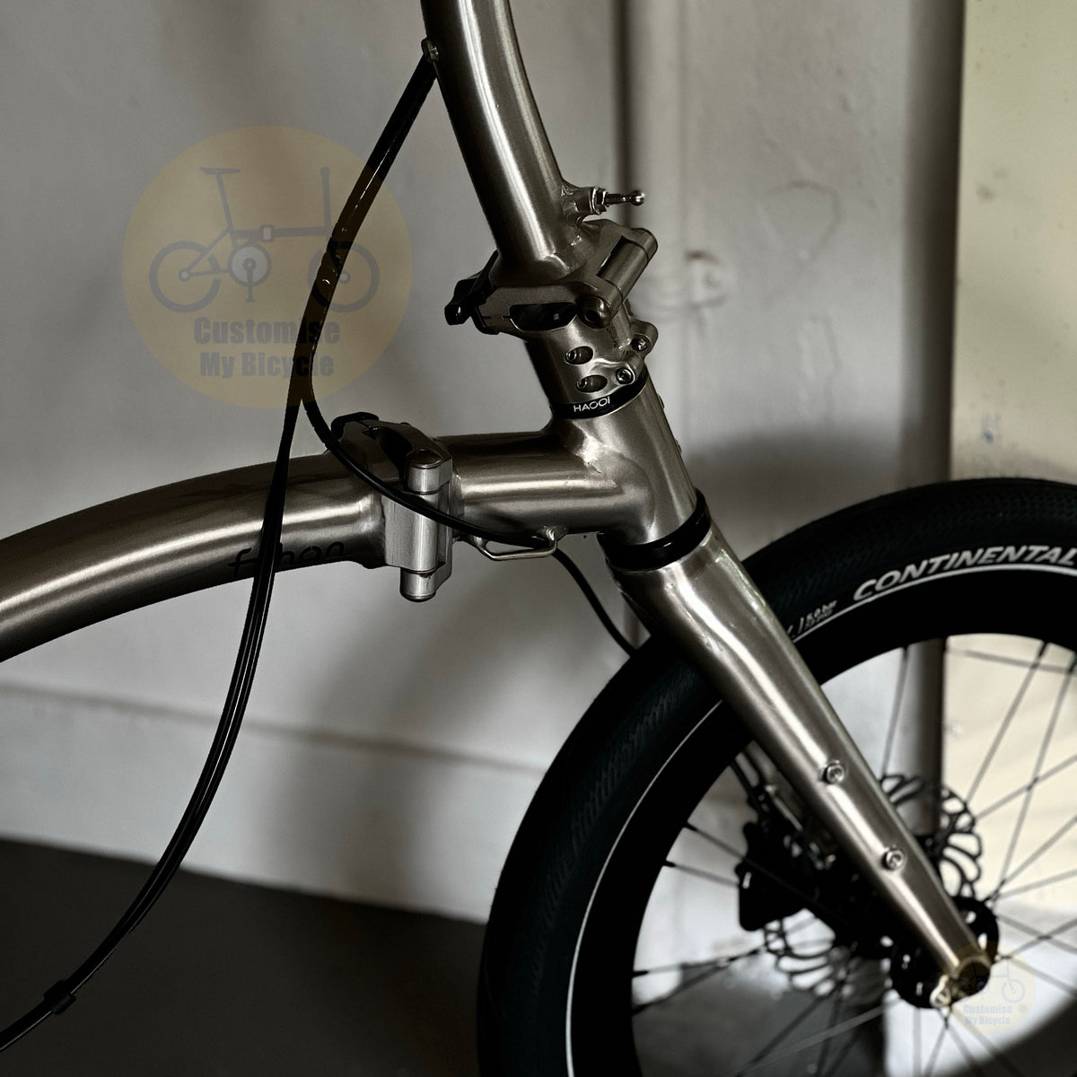 Close-up of a metallic silver bicycle frame and front wheel with a black Continental tire, photographed indoors against a light wall.