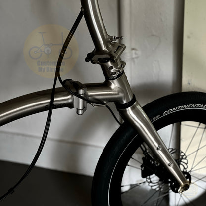 Close-up of a metallic silver bicycle frame and front wheel with a black Continental tire, photographed indoors against a light wall.