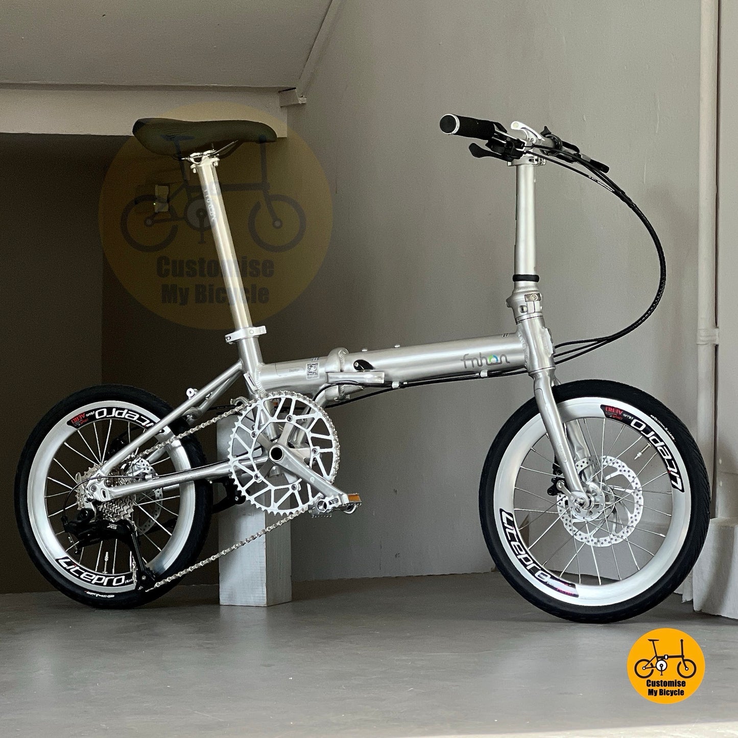Lower side view of Fnhon Zephyr 18-inch folding bike in polished silver, displayed on wooden deck with city skyline at sunset.
