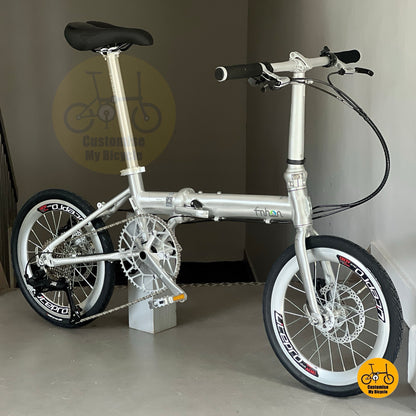 Angled view of Fnhon Zephyr polished silver folding bicycle, emphasizing smooth frame curves and sunset lighting effect.