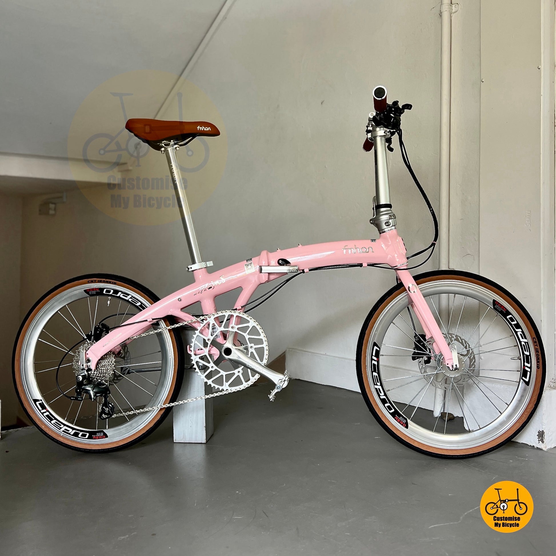 Pink bicycle with brown seat on a stand against a plain wall.